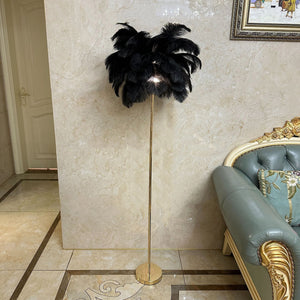 Stehlampe mit schwarzen Straussenfedern und goldenem Ständer neben einem blauen Sofa und beiger Wand