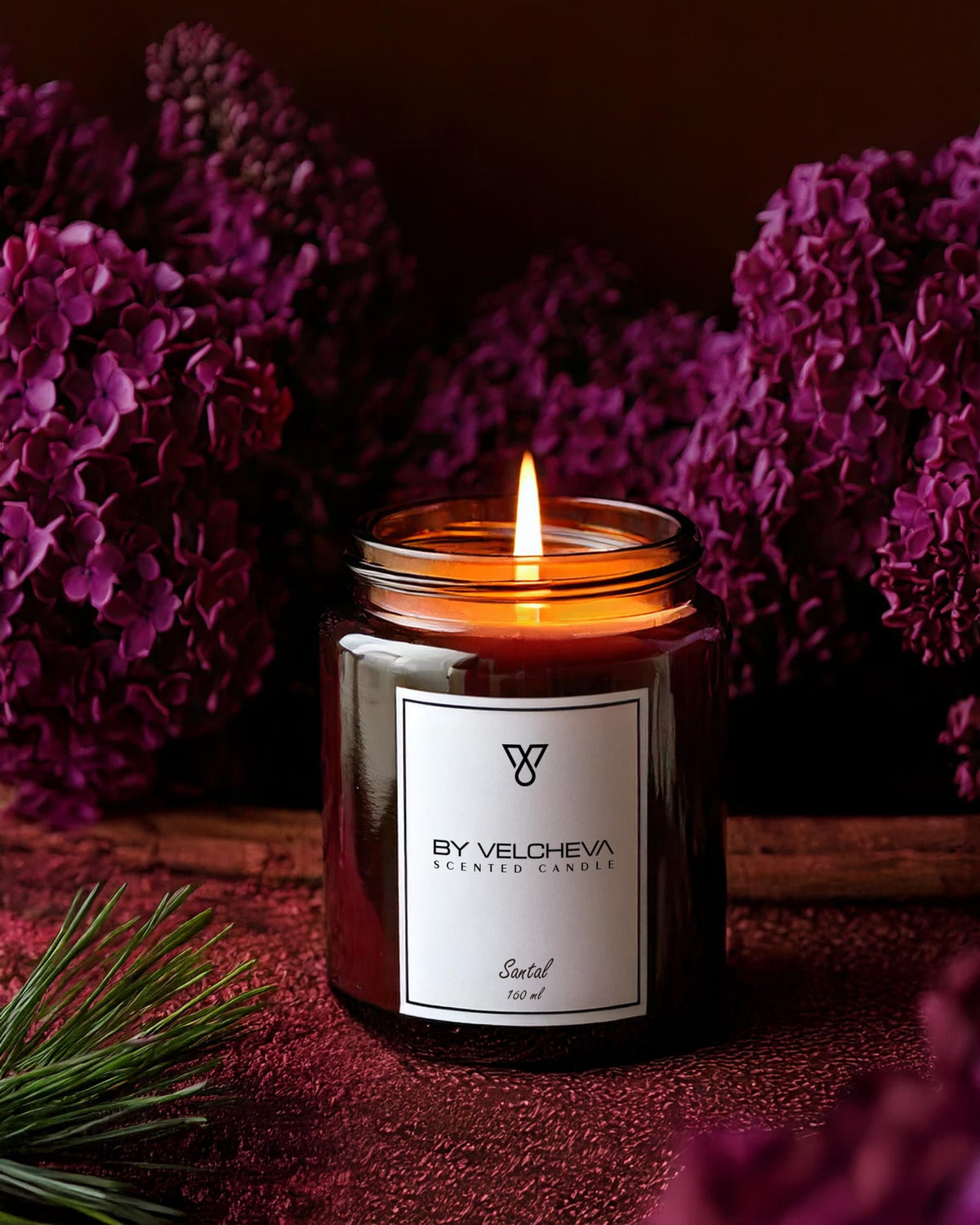 Brennende Duftkerze in einem braunen Glas mit lila Blumen im Hintergrund