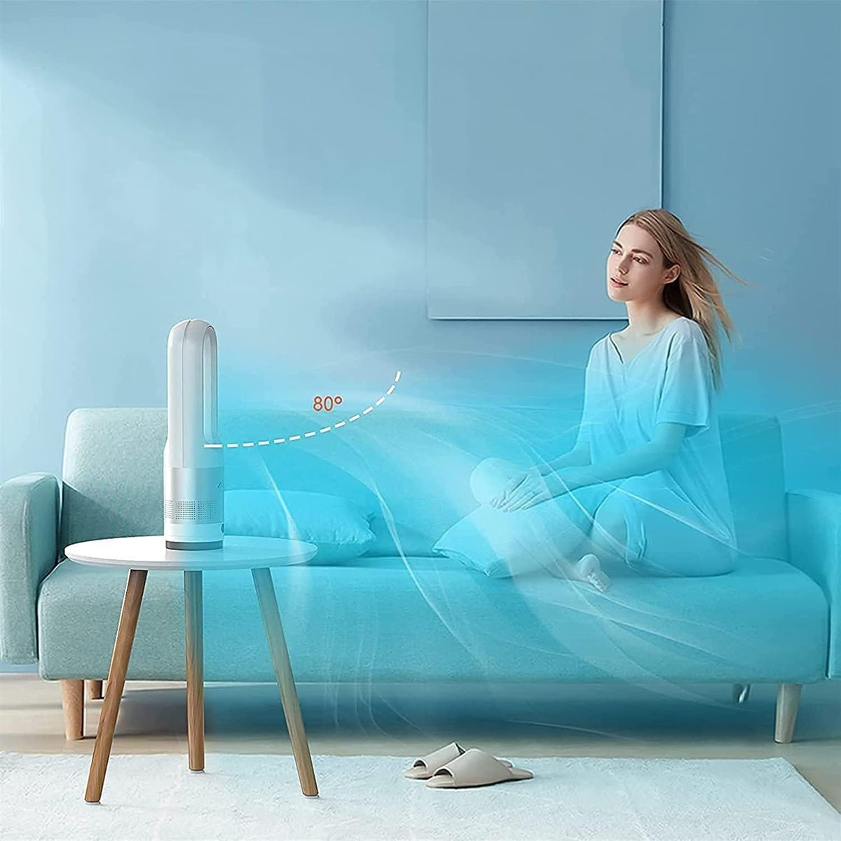 Grauer Turmventilator in Form eines Ovals auf einem kleinen Tisch und einem Sofa mit Person im Hintergrund