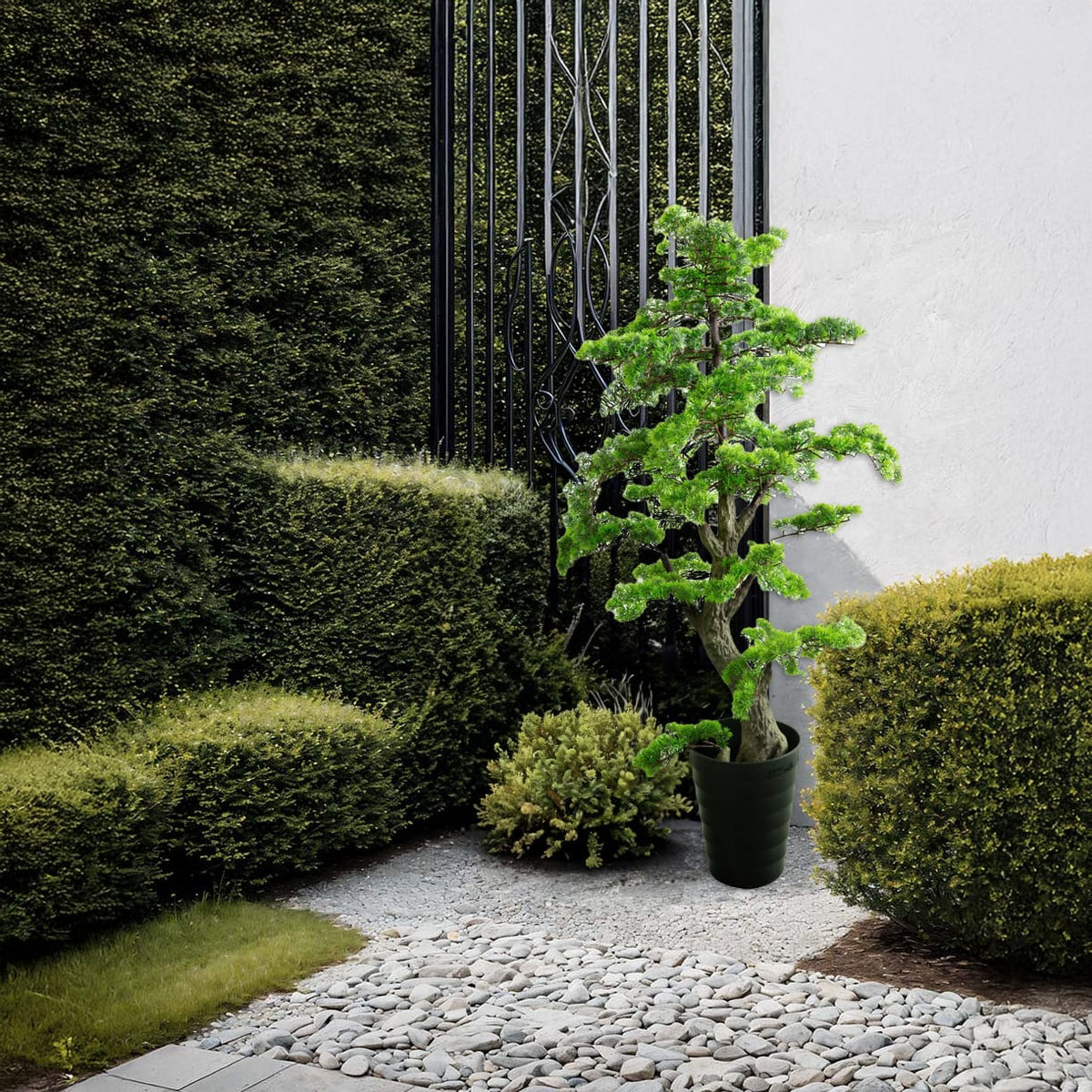 Künstlicher, detaillierter Bonsai mit schwarzem Topf in einem Aufstellbeispiel neben Gebüsch und Steinboden