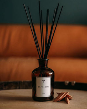 Raumduft mit Holzstäbchen in einem braunen Glas neben klein gehacktem Holz