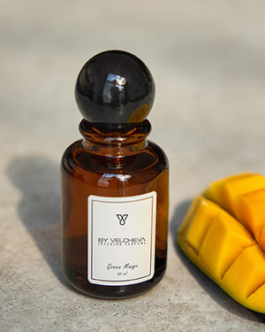 Raumduft Spray in kleiner, braunen Glasflasche mit schwarzem Deckel neben einem geschnittenem Stück Mango